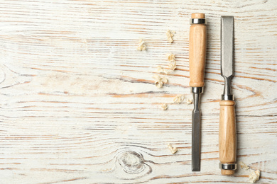 Chisels and shavings on white wooden background, flat lay with space for text. Carpenter's tools