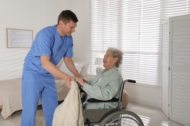 Caregiver assisting senior woman in wheelchair indoors. Home health care service