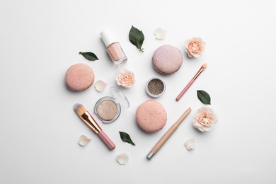 Flat lay composition with makeup products, roses and macarons on white background