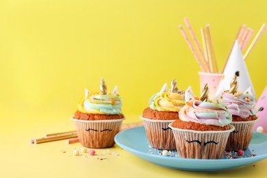 Photo of Cute sweet unicorn cupcakes and party items on yellow background, space for text