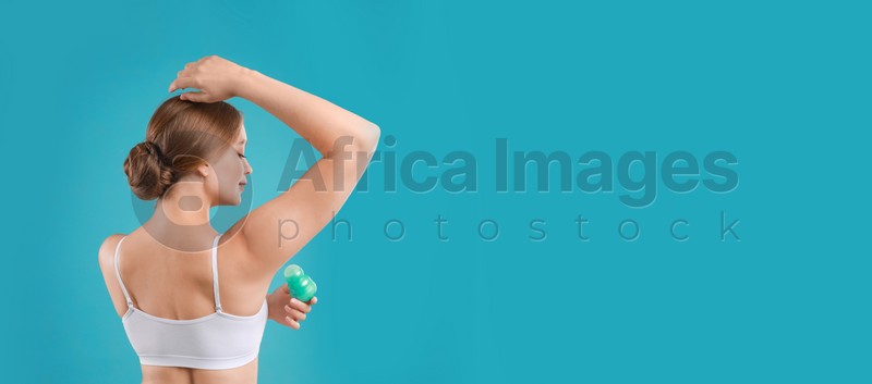 Young woman applying deodorant to armpit on turquoise background, space for text. Banner design