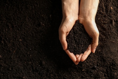 Woman with handful of soil outdoors, top view. Space for text