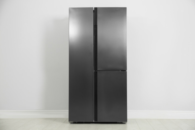 Modern refrigerator near light grey wall. Home appliance