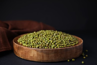 Wooden bowl with green mung beans and napkin on black background, closeup