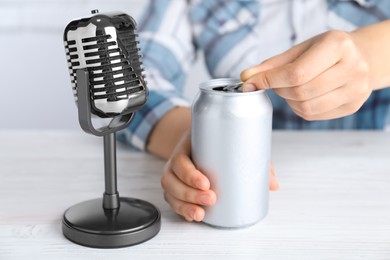 Woman making ASMR sounds with microphone and can at white table, closeup