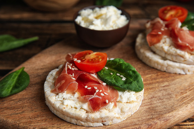 Puffed rice cake with prosciutto, tomato and basil on wooden board, closeup