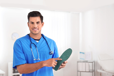 Handsome male orthopedist showing insole in clinic