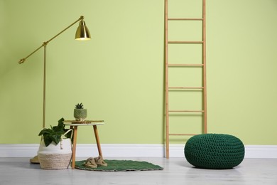 Stylish room interior with comfortable knitted pouf and plants near light green wall