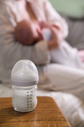 Mother and her little baby at home, focus on bottle of milk. Space for text