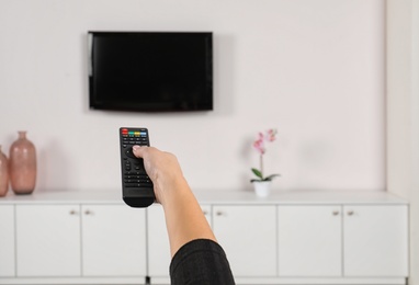 Woman switching channels on TV set with remote control at home