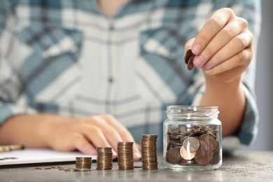 Woman putting money into glass jar at table, closeup