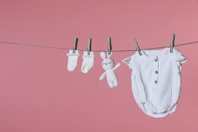 Different baby clothes and bunny toy drying on laundry line against pink background