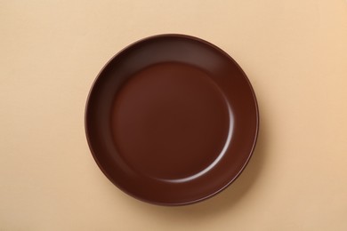 Photo of Empty brown ceramic plate on pale orange background, top view