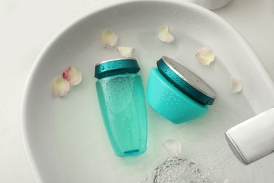 Hair care cosmetic products with flower petals and water in sink, above view