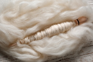 Soft white wool and spindle on wooden table, closeup