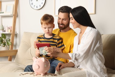 Happy family with calculator putting money into piggy bank at home