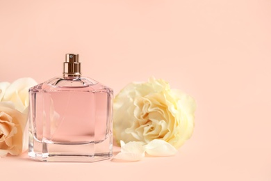 Bottle of perfume and beautiful flowers on beige background. Space for text