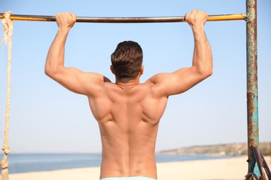 Man with slim body doing pull-ups
on beach