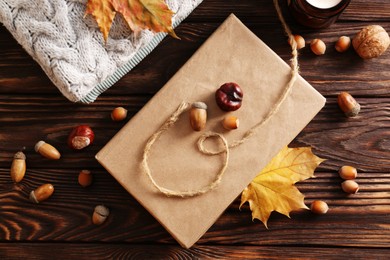 Photo of Book with autumn leaf as bookmark, acorns, scented candle and warm sweaters on wooden table, flat lay