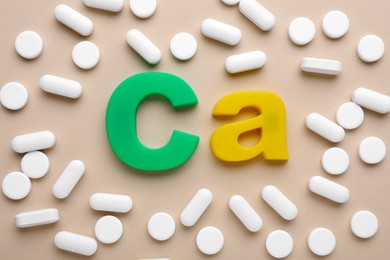 Pills and calcium symbol made of colorful letters on beige background, flat lay