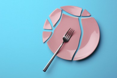 Pieces of broken ceramic plate and fork on light blue background, flat lay. Space for text