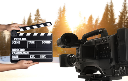 Modern video camera and assistant with clapperboard outdoors, closeup. Cinema production 