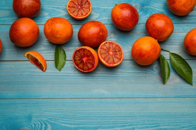Many ripe sicilian oranges and leaves on light blue wooden table, flat lay. Space for text