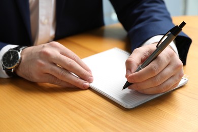 Left-handed man writing in notebook at wooden desk, closeup