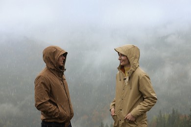 Man and woman in raincoats talking outdoors during rain