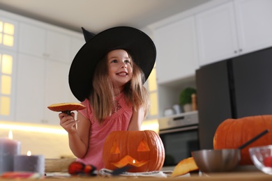 Little girl with pumpkin jack o'lantern at table in kitchen. Halloween celebration