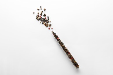 Glass tube with peppercorns on white background, top view