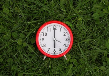 Red alarm clock on green grass outdoors, top view