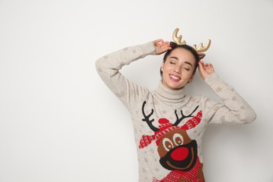 Young woman in Christmas sweater and deer headband on white background, space for text