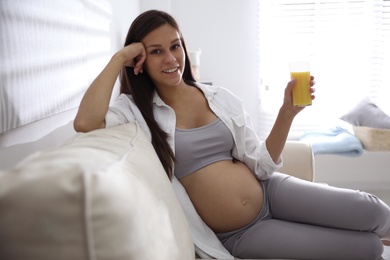 Young pregnant woman with glass of juice in living room. Taking care of baby health