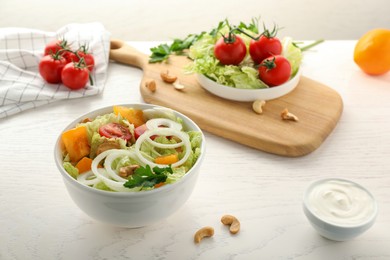 Photo of Bowl of delicious salad with Chinese cabbage, tomatoes and onion on white wooden table