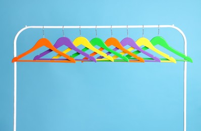 Bright clothes hangers on metal rack against light blue background