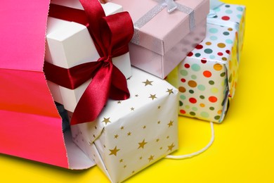 Photo of Pink paper shopping bag full of gift boxes on yellow background, closeup