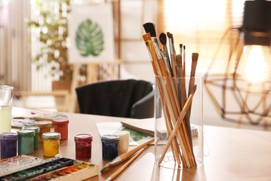 Photo of Paints and brushes on wooden table in art studio