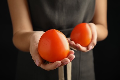 Woman holding delicious fresh persimmons on black background, closeup