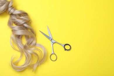 Professional hairdresser scissors, hair strands and space for text on yellow background, flat lay. Haircut tool