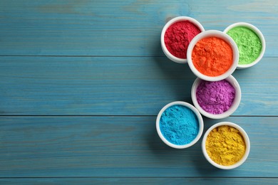 Colorful powder dyes on light blue wooden background, flat lay with space for text. Holi festival