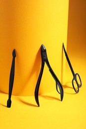 Photo of Manicure scissors, cuticle nipper and pusher on yellow background