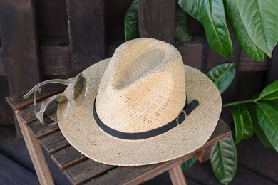 Photo of Stylish hat and sunglasses on wooden stool near fence. Beach accessories