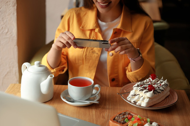 Young blogger taking picture of tea at table in cafe, closeup
