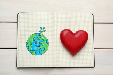 Happy Earth Day. Notebook with drawing of planet and decorative heart on white wooden table, top view