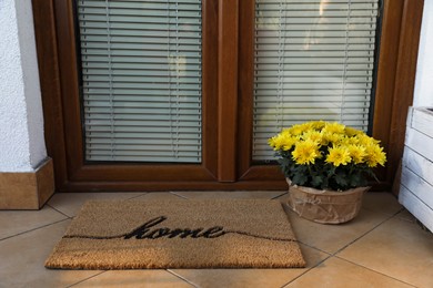 Photo of Doormat with word Home and flowers near entrance outdoors