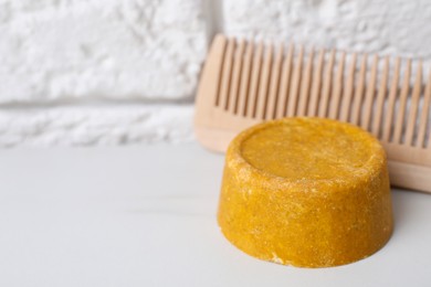Orange solid shampoo bar and comb on white table, closeup. Space for text
