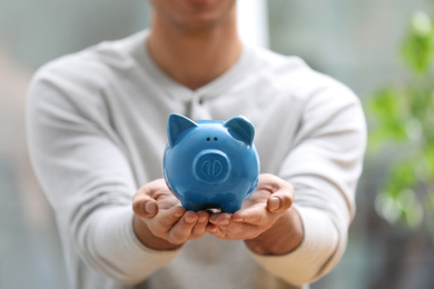Man holding piggy bank against blurred background, closeup