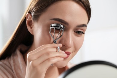 Photo of Young woman using eyelash curler near mirror, closeup