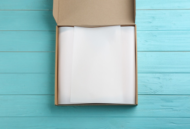 Cardboard box with parchment on light blue wooden background, top view